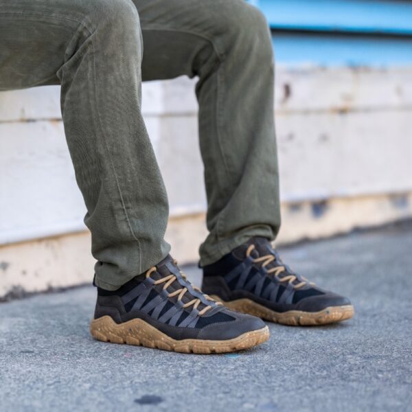 Koel Barefoot Raxo dark grey - mężczyzna siedzący na murku, nogi w spodniach, buty na stopach